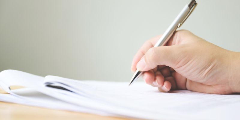 A hand gripping a pen, poised above a sheet of paper, engaged in the act of writing.