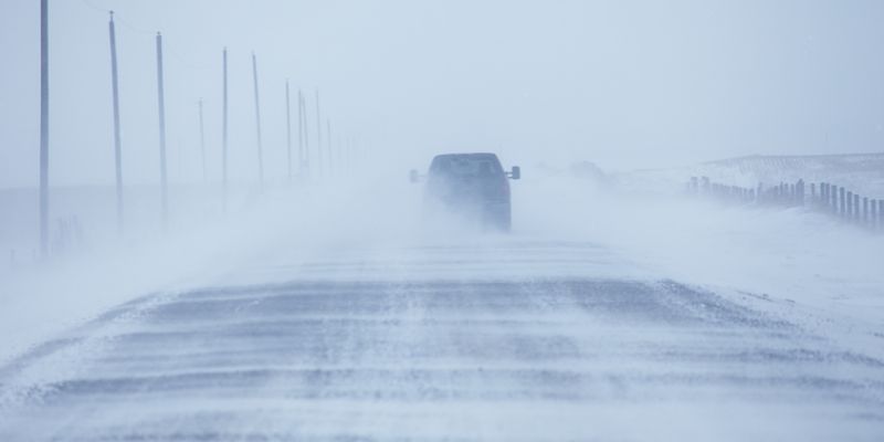 A truck navigates a snowy road, surrounded by a winter landscape blanketed in fresh snow.