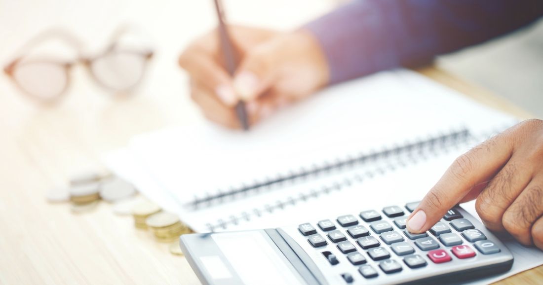 A person operating a calculator while holding a pen, reviewing figures on a sheet of paper.
