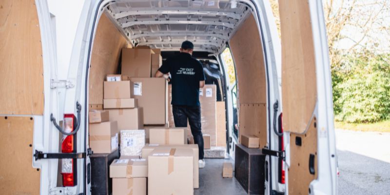 A man is placing boxes into a van, preparing for transportation or moving tasks.