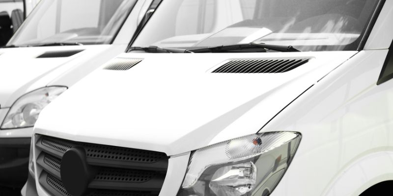 A row of white vans neatly parked in alignment, showcasing their uniformity and organisation.