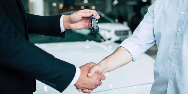 Two men shaking hands in front of a car, symbolising agreement and partnership in a professional setting.