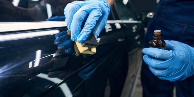 A man wearing blue gloves is meticulously polishing a car's surface to enhance its shine and appearance.