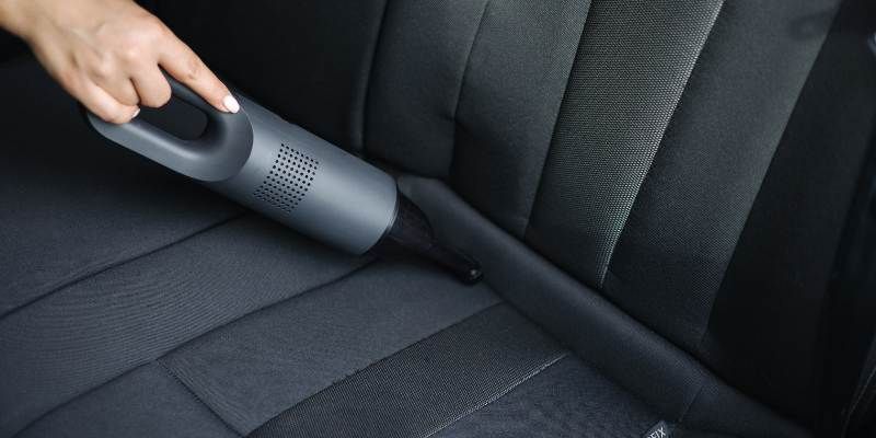A person vacuuming a car seat, ensuring a clean and tidy interior.