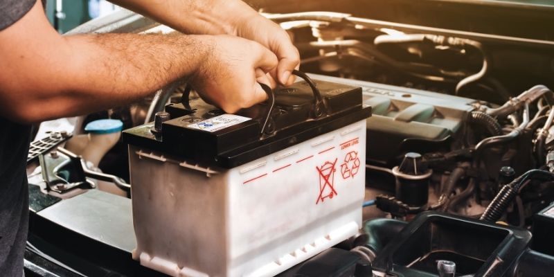 A person holding a car battery in their hand, ready to replace.