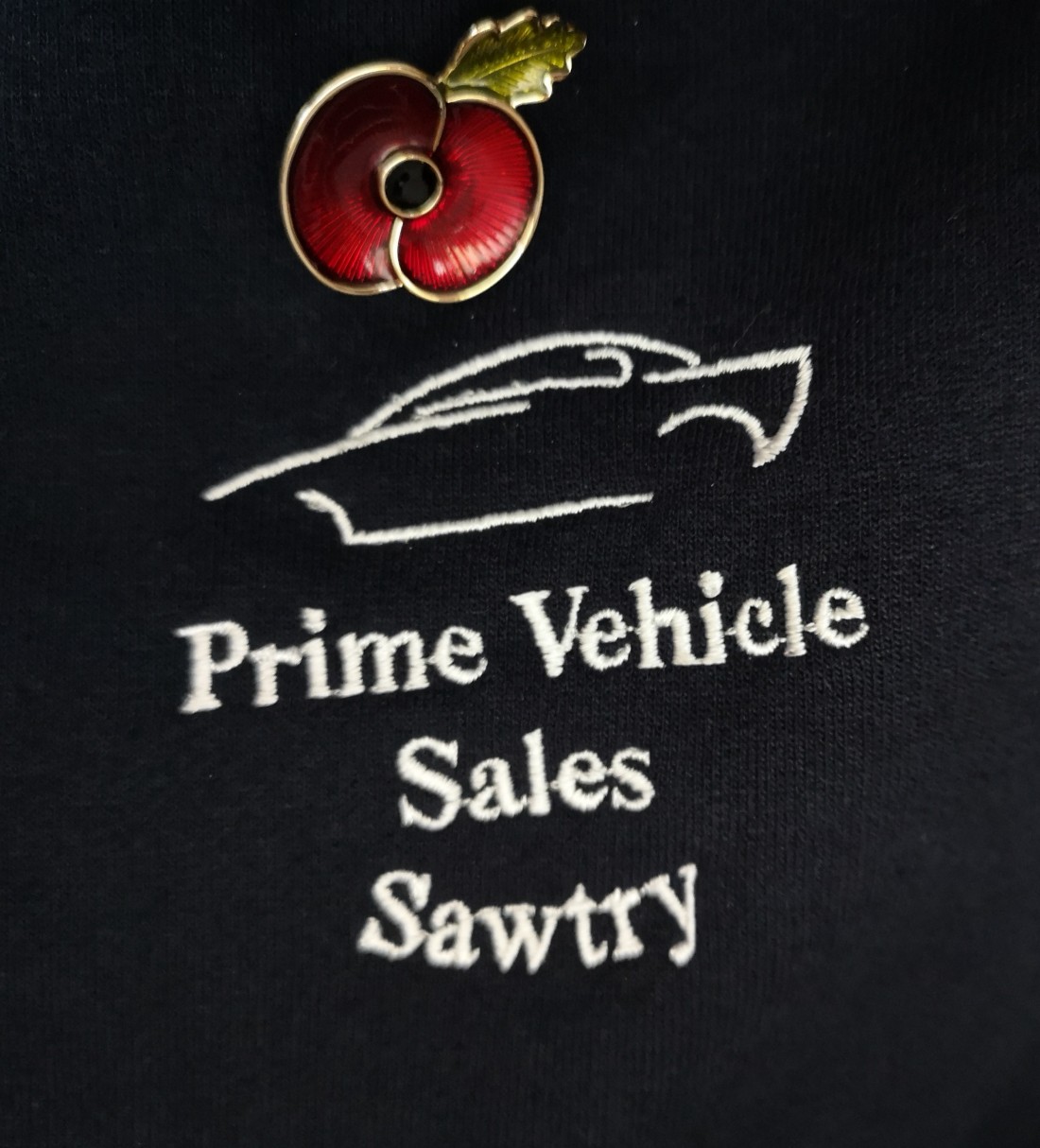 A black shirt featuring a poppy and the Prime Vehicle Sales logo.