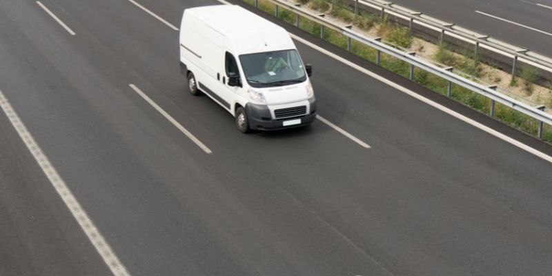 A white van traveling along a highway under a clear blue sky.