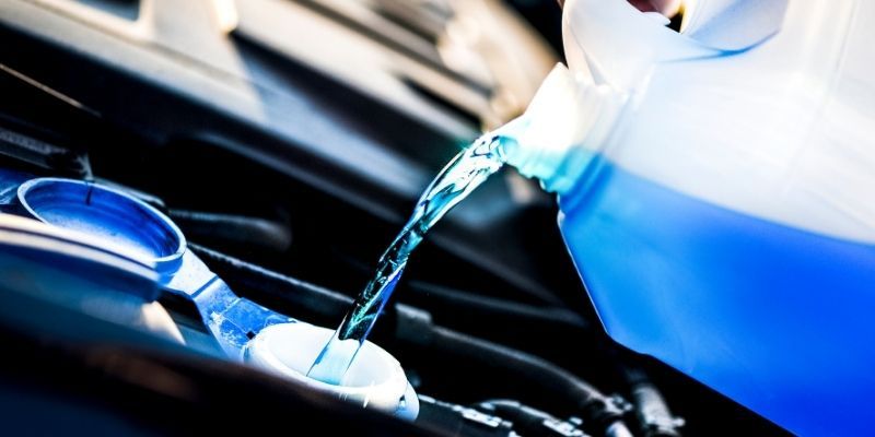 A person carefully pours liquid into a car engine, ensuring proper maintenance and functionality of the vehicle.