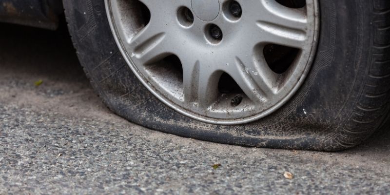 A flat tyre lies on the ground beside a parked car, indicating a need for repair or replacement.