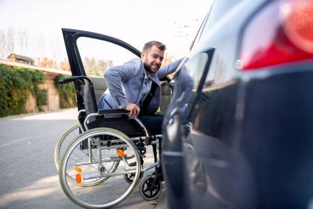 A male wheelchair user smiling as the camera as he gets into the passenger side of a car.