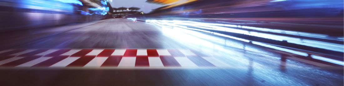 A blurred racing track, indicating speed, with bright lights and a red and white finish line.