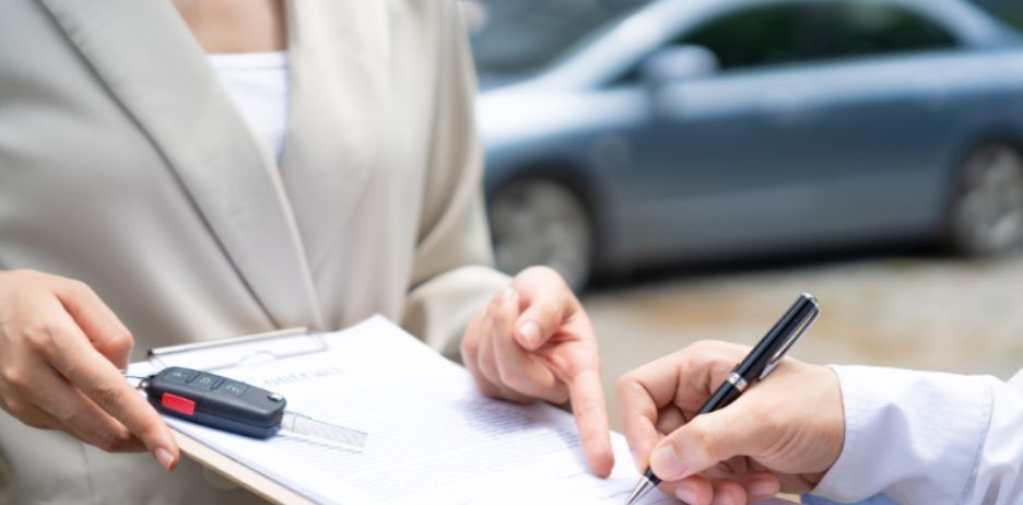 Two people completing paperwork for a car transaction.
