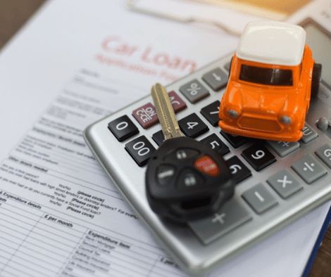 Car loan paperwork with a calculator, orange toy car and car keys sat on top.