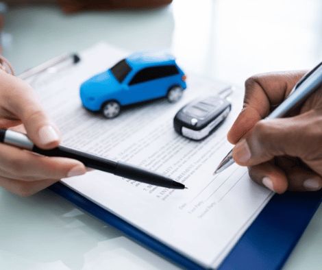 Two people signing paperwork, with a blue toy car and car keys sat on top