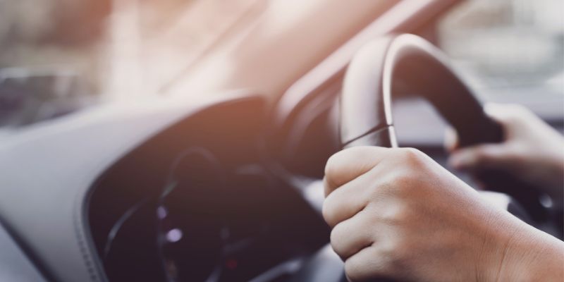 An Individual driving a car and holding the steering wheel
