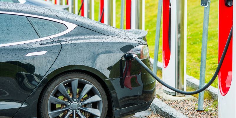 Electric car charging at a station, plugged in and parked on a rainy day, highlighting eco-friendly transportation.