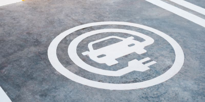 Electric vehicle charging station symbol painted on pavement, designating a reserved parking space for EVs.