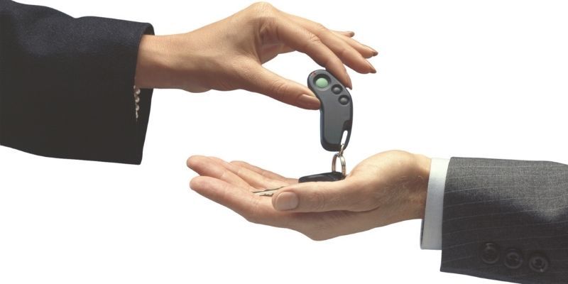 A person handing over car keys to another individual, symbolising car ownership, a rental agreement, or a car finance transaction.