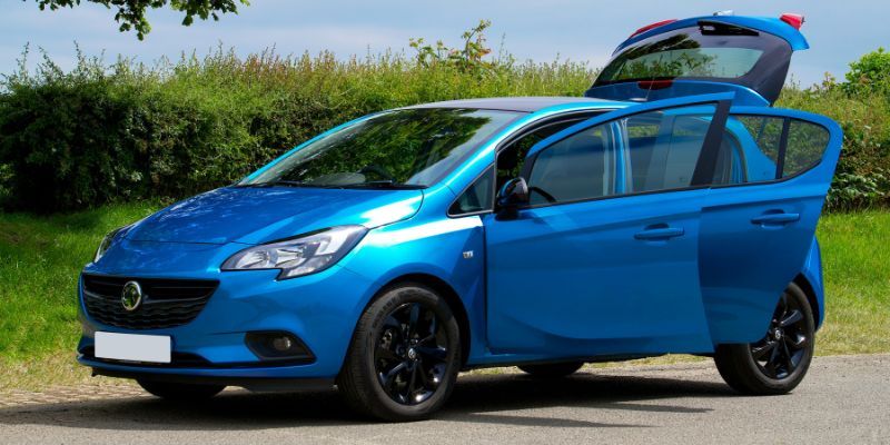 A blue Vauxhall car parked with an open boot. 