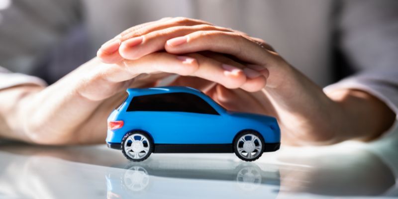 A person's hands over a small blue toy car, symbolizing protection and care.