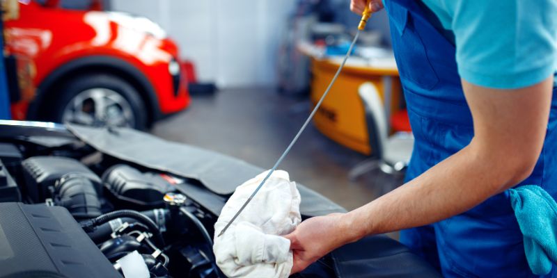 A man checking the car motor oil using an oil level indicator tool.