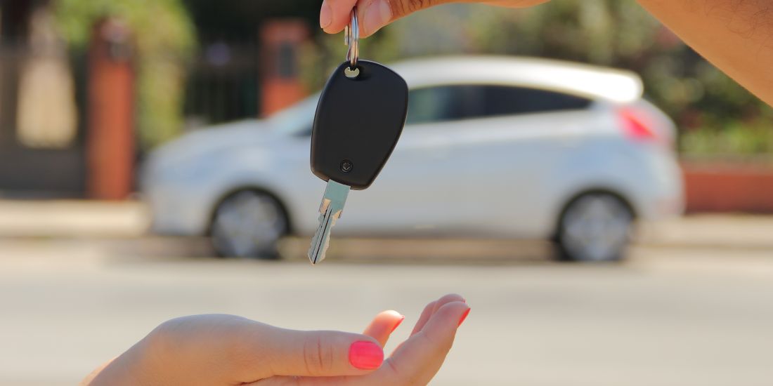 a womans hand, palm side up, with a car key dangling over it ready to be clasped.