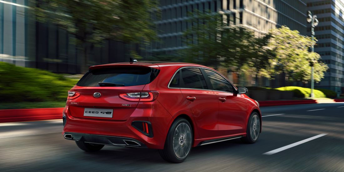 A red Kia Cee'd gracefully cruises down a city street, showcasing the sleek design.
