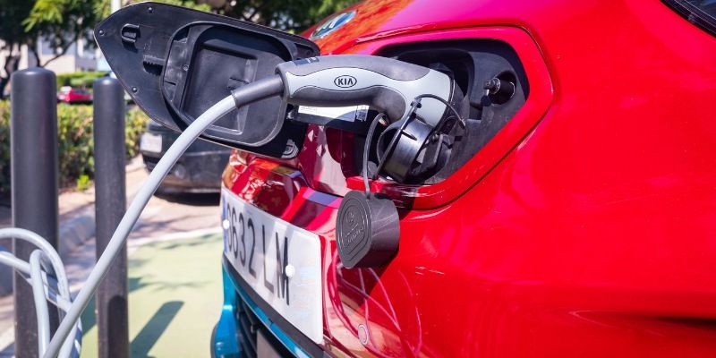 A red electric Kia car charging at a Kia charging point.