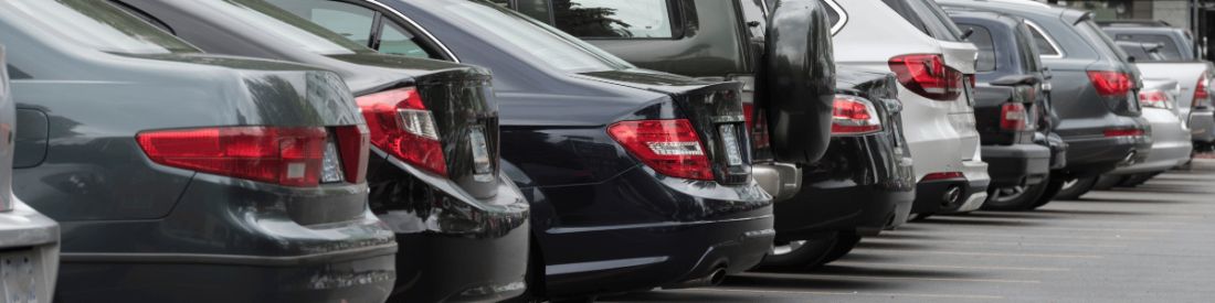 Rear view of multiple cars parked closely together in a car dealership lot.