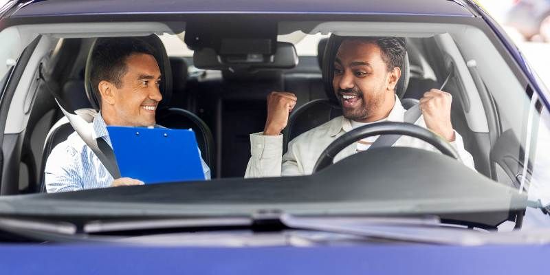 An examiner showing a driver their test results inside of their car, they are smiling and celebrating