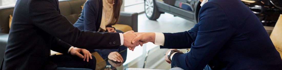 Two men shaking hands in a car showroom, discussing car finance