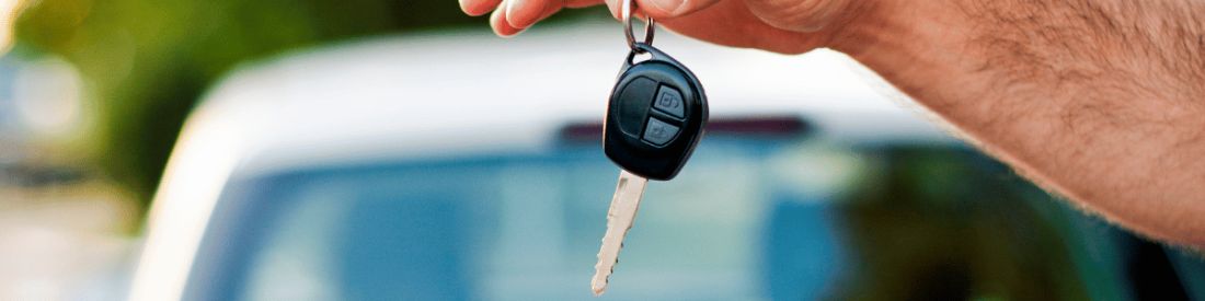 Person holding a car key in front of a blurred car, symbolising car ownership or purchase.