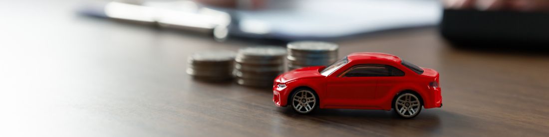 In focus red toy car with a stack of blurred coins increasing in size order on a table in the background