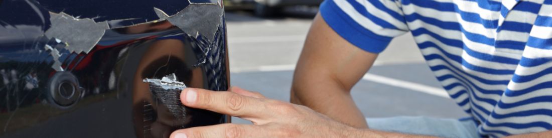 Man inspecting scratched car bumper for insurance or repair claim opportunity.