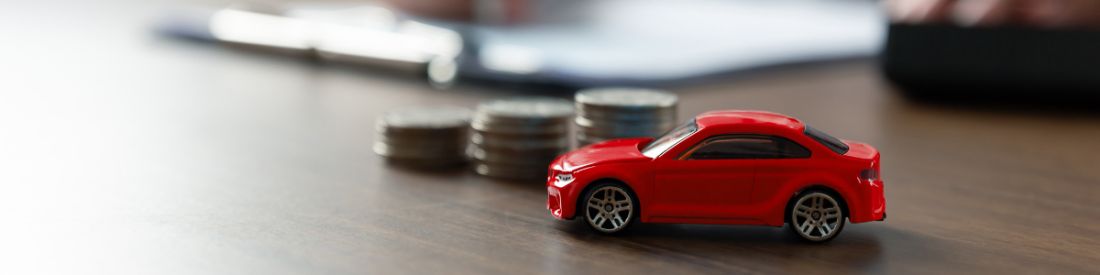 Red toy car placed in front of a stack of coins, indicating car finance
