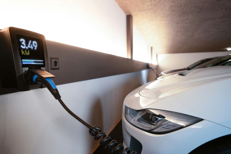 A white car plugged in at an electric charging point.