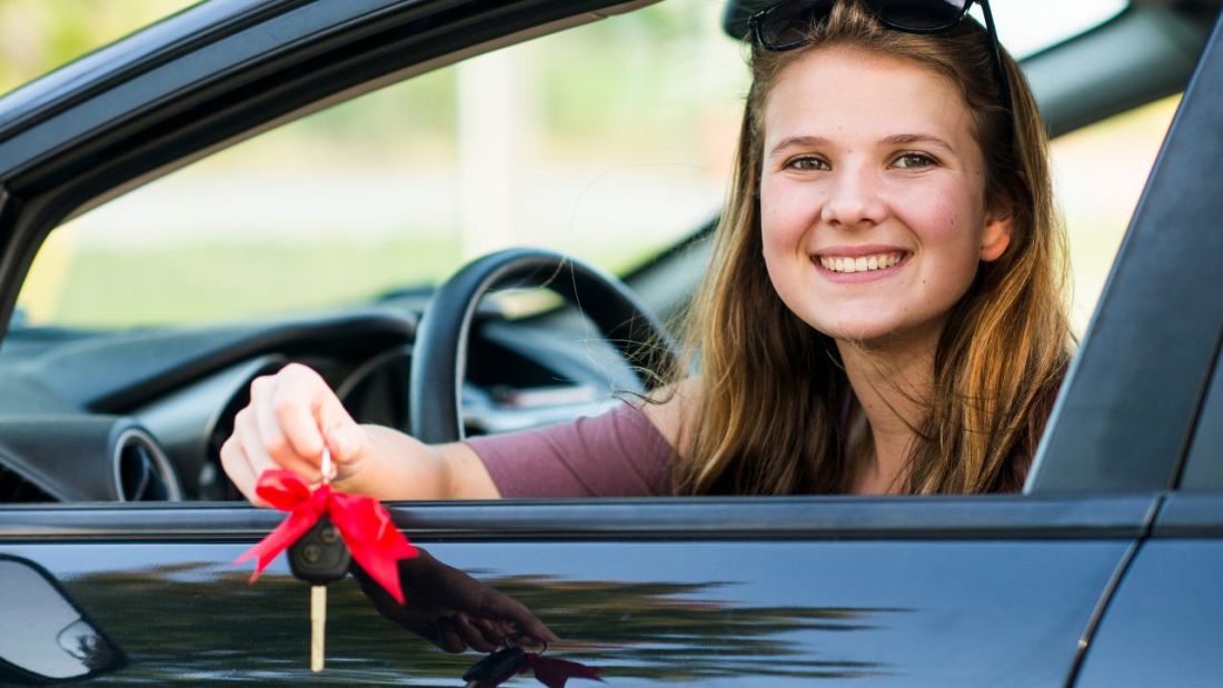 A young girl in the drivers seat, in her hand is a car key with a red bow on.