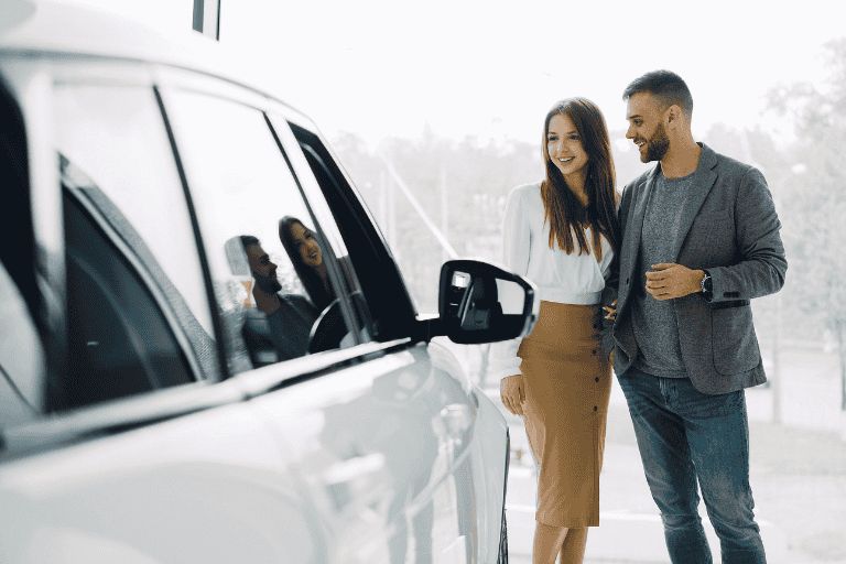 A young couple, looking at a white car inside a showroom.
