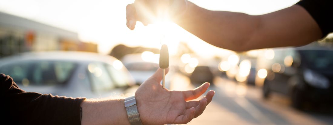 Person handing over car keys during a vehicle purchase at a dealership.