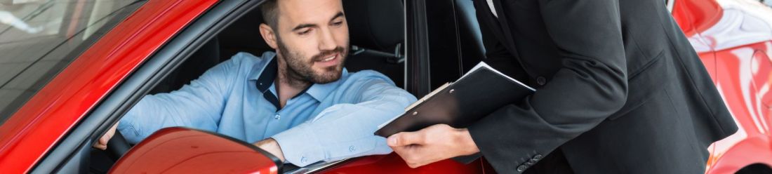A brunette male looking left out of his car window at a man holding a clipboard