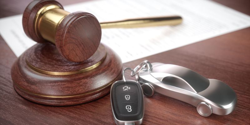 A wooden gavel placed next to a set of car keys and a metallic car-shaped keychain.