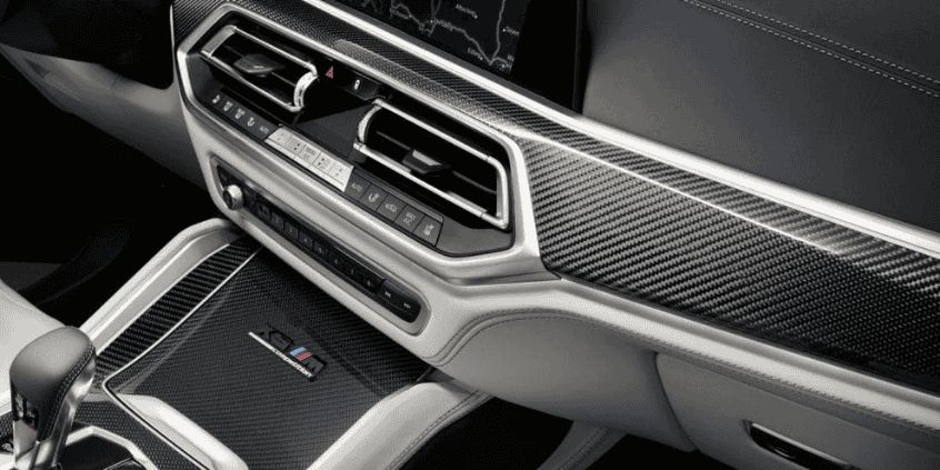 A close-up view of a luxury car's interior, featuring a carbon fibre dashboard, sleek air vents, and high-quality detailing with a gear selector in the foreground.