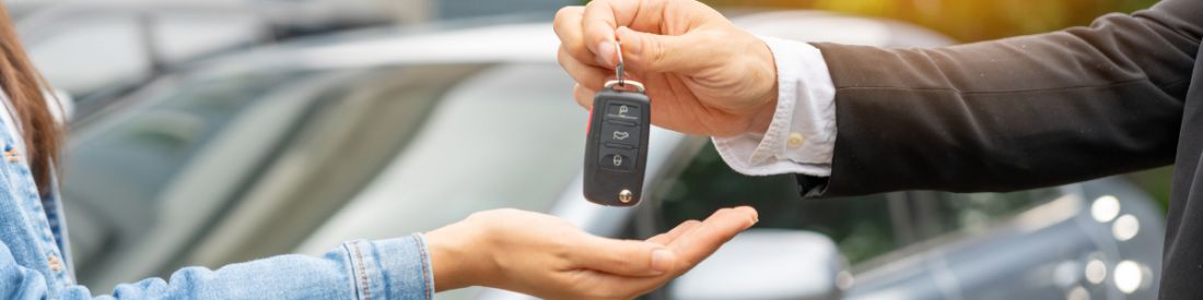 A lady in a denim jacket is accepting car keys from a car sales man.