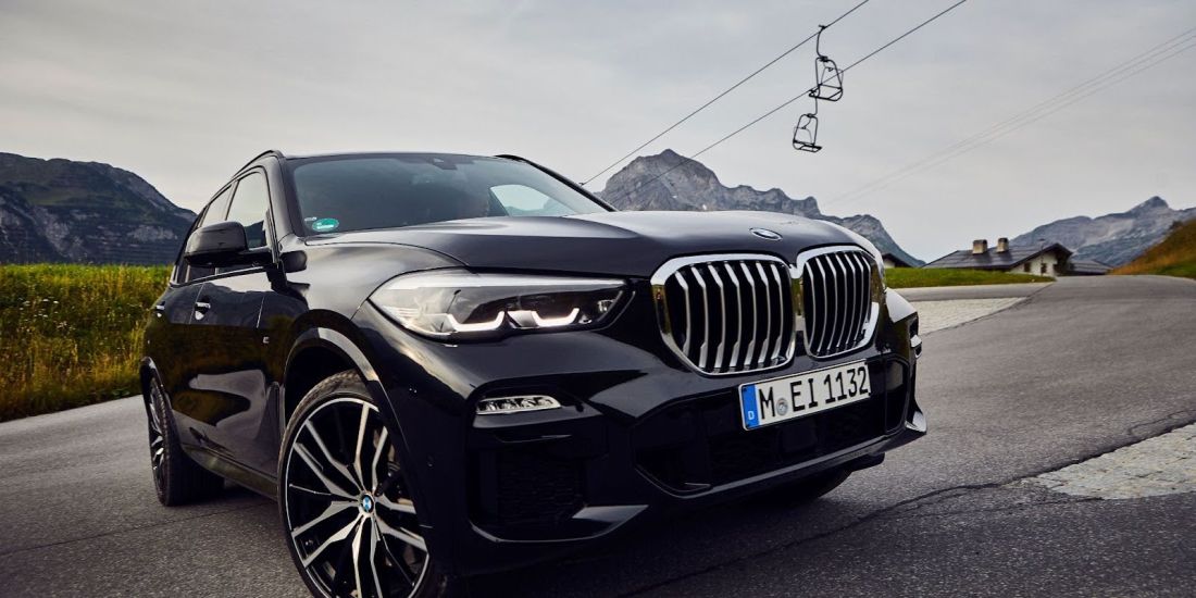 A BMW X5 navigates a winding mountain road, showcasing its performance and elegance in a scenic landscape.