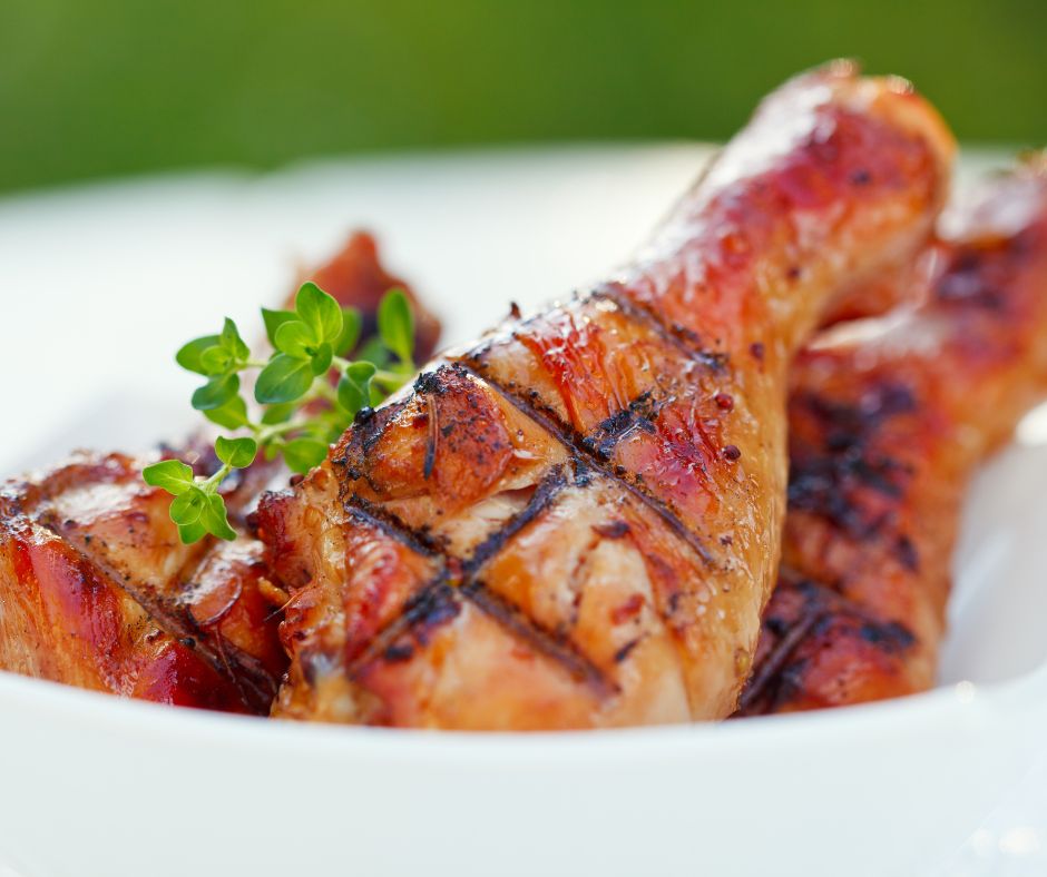 Barbequed chicken with grill marks, in a bowl with some greens. 