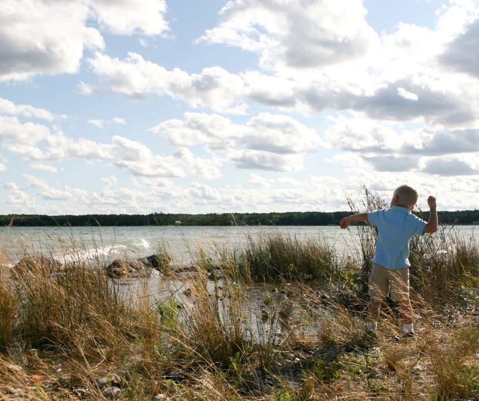A child standing at the lake shore. He is about to throw a stone in the lake,.