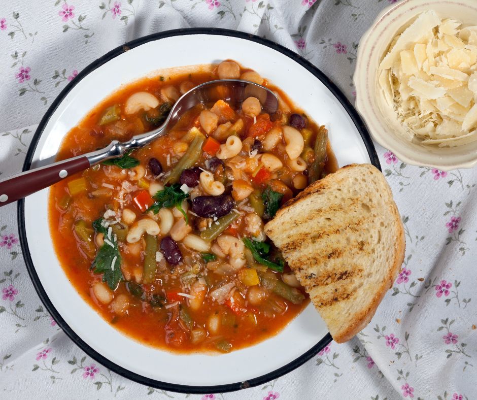 A bowl of minestrone soup with toasted bread on the side. 