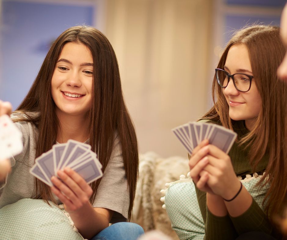 Two teenage girls smiling and playing a card game,