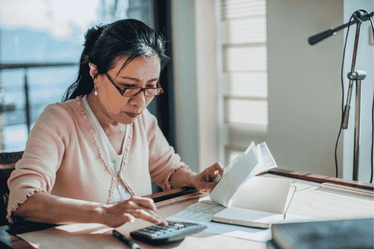 A woman is sat at her desk with paperwork, calculating which finance is best for her.