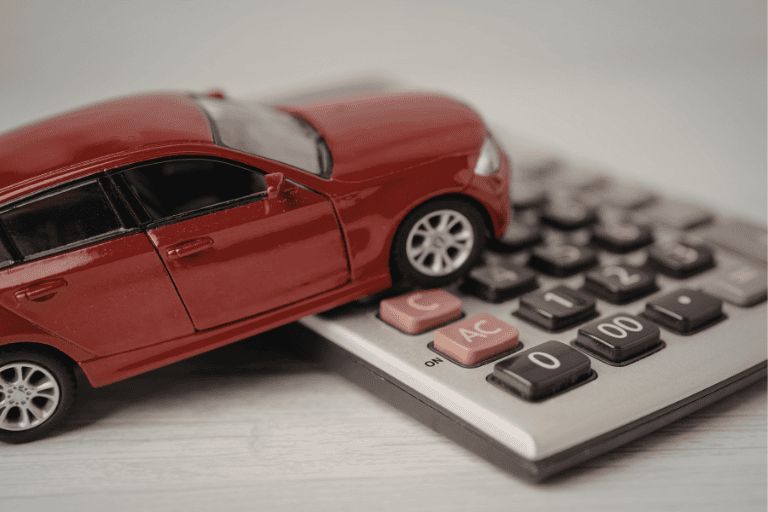 A red toy car is resting on top of a calculator on a desk.